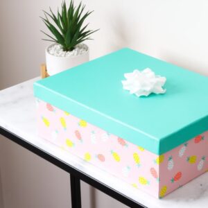 A colorful box with a blue lid and a white bow on a desk next to a plant.