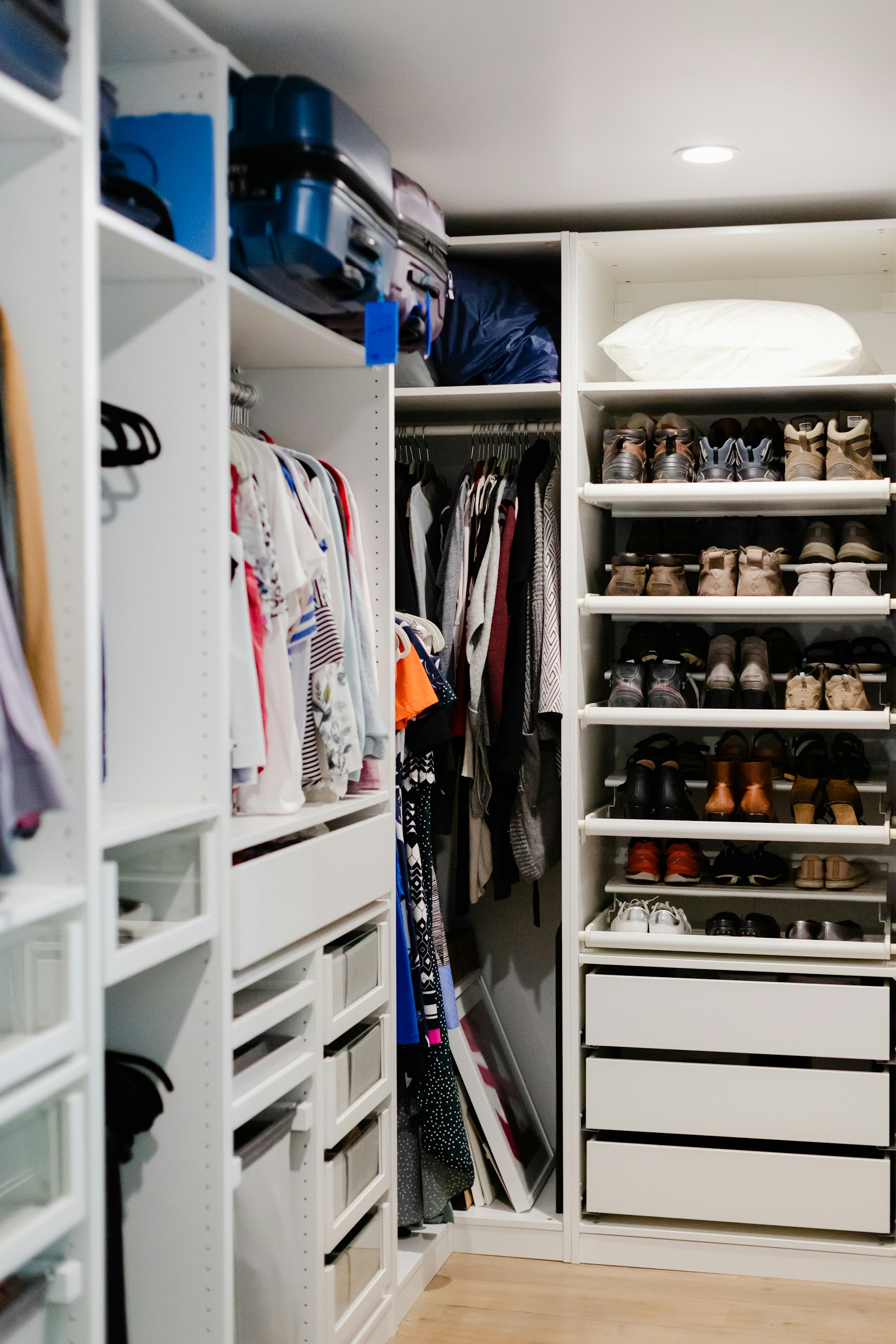 Organized walk-in closet with clothing, shoe shelves, drawers, and upper storage